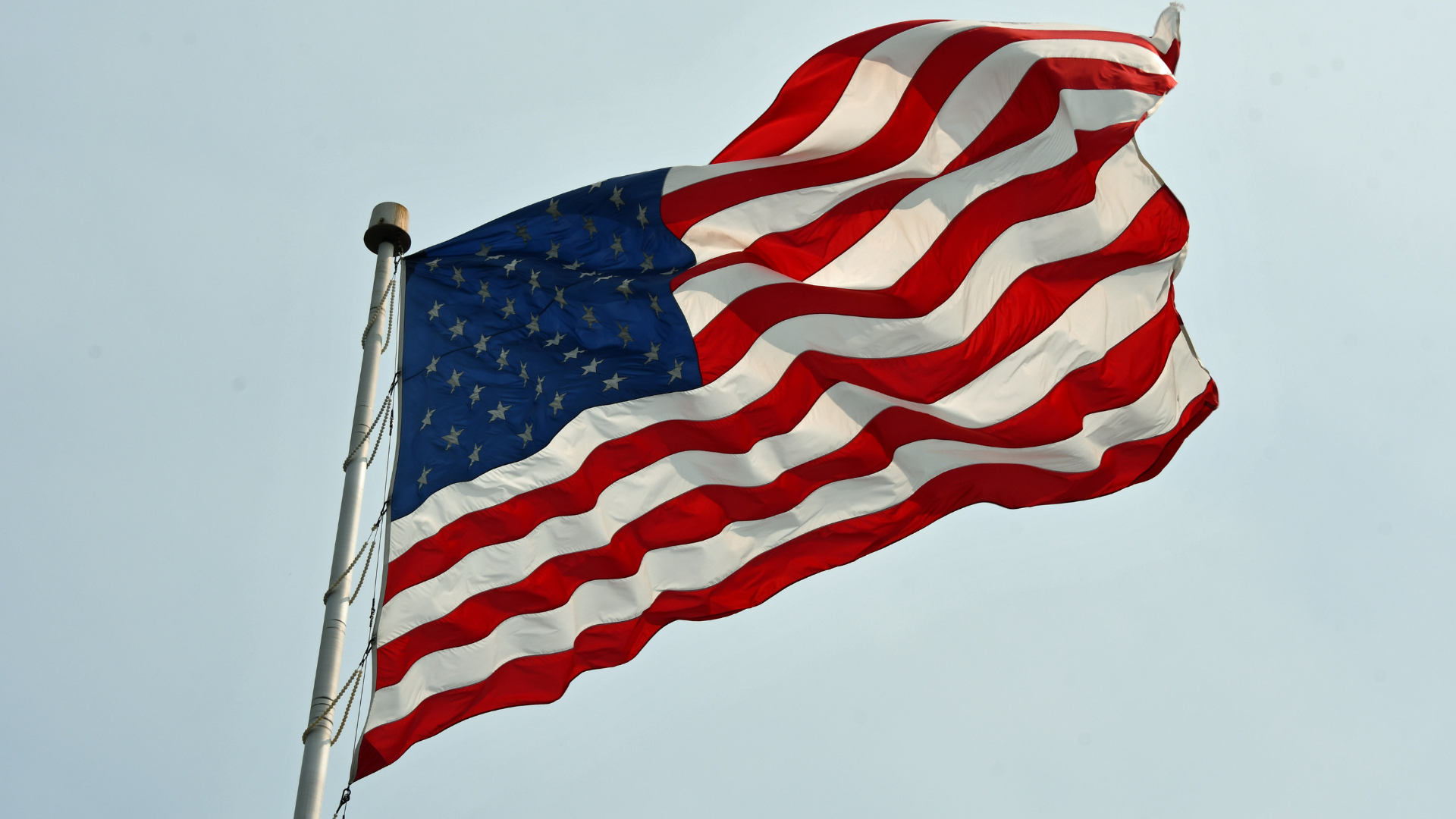 An image of the American flag flowing in the wind against the sky. A symbol of independence day