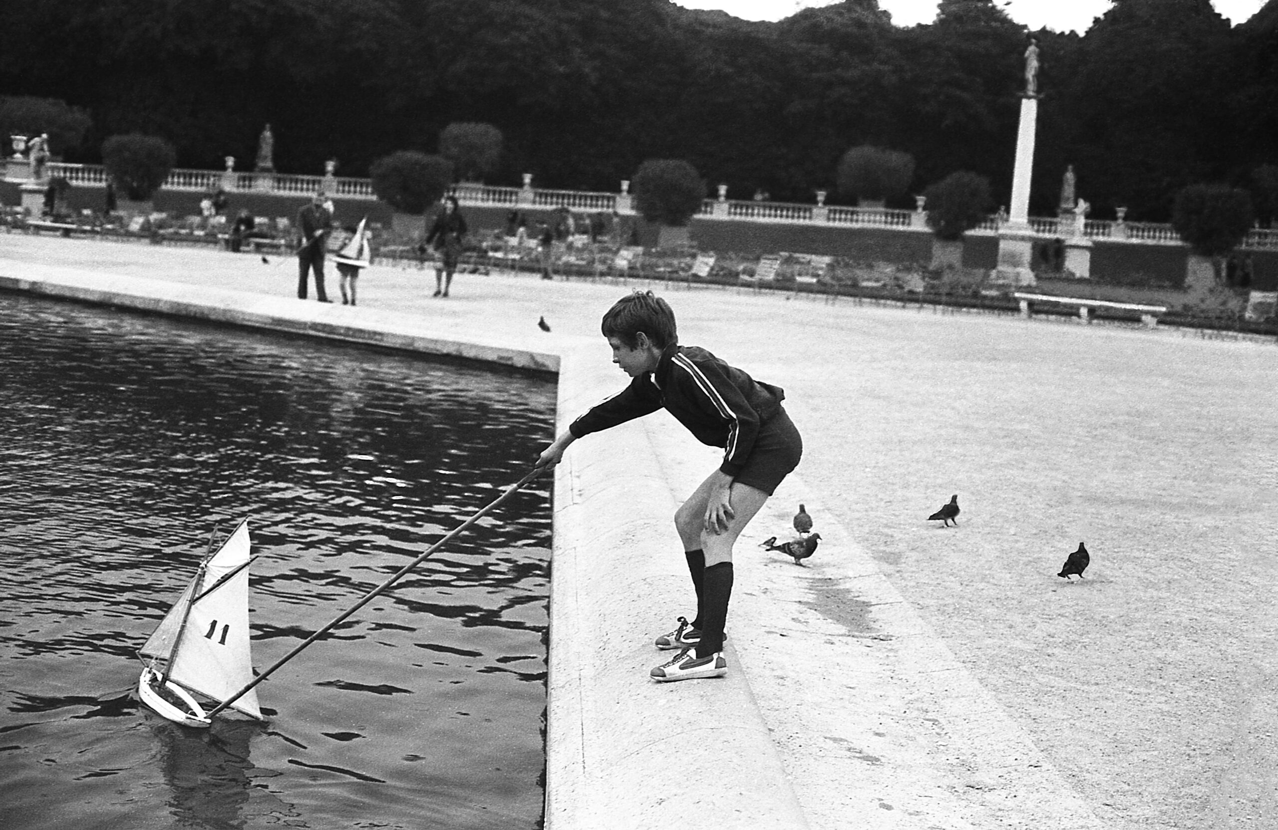 Child playing with model sailboat in park pond