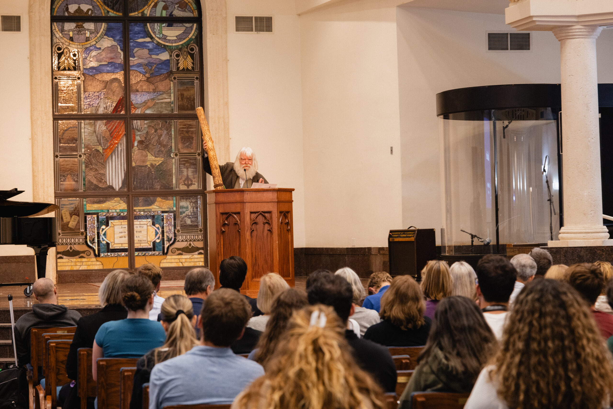 Malcolm Guite holds a rainstick while lecturing in PBA DeSantis Family Chapel.